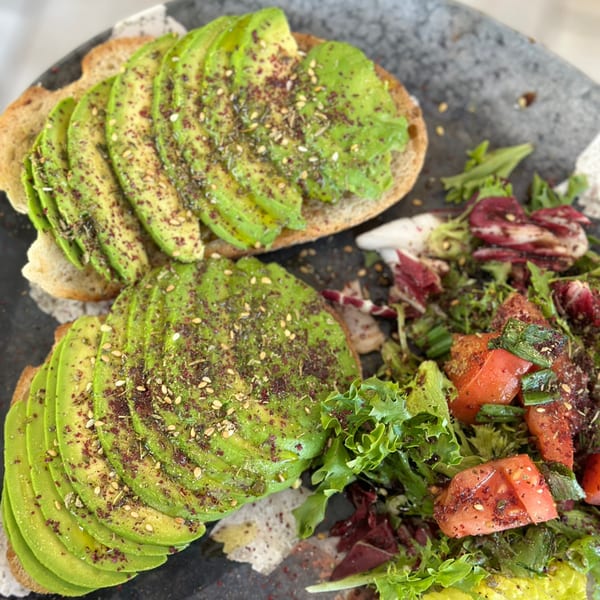Two avocado toasts topped with spices and sesame seeds, served with a side salad.