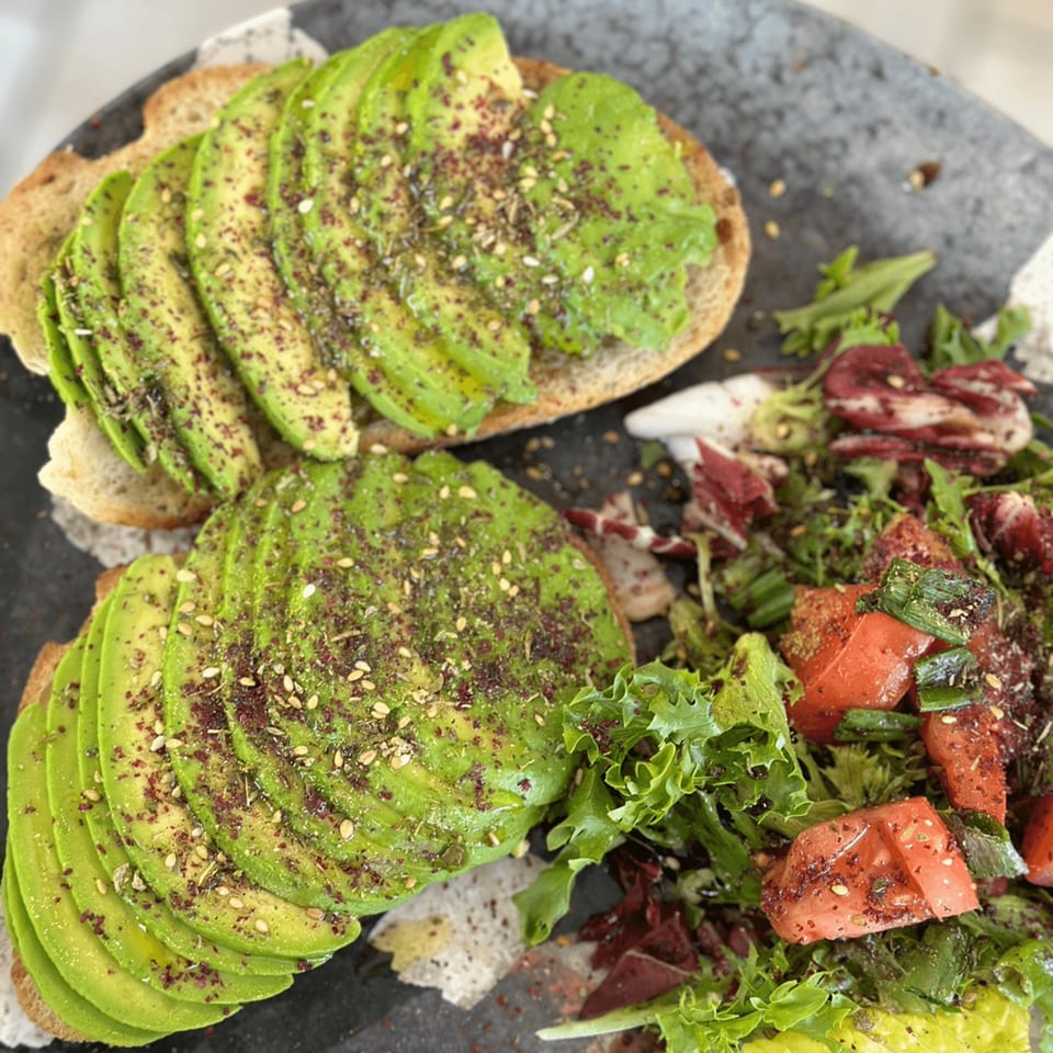 Avocado toast with spices and a side salad with tomatoes and greens on a dark plate.