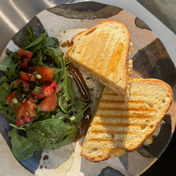 Grilled sandwich with grill marks, served with a side salad of spinach, tomatoes, and balsamic glaze.