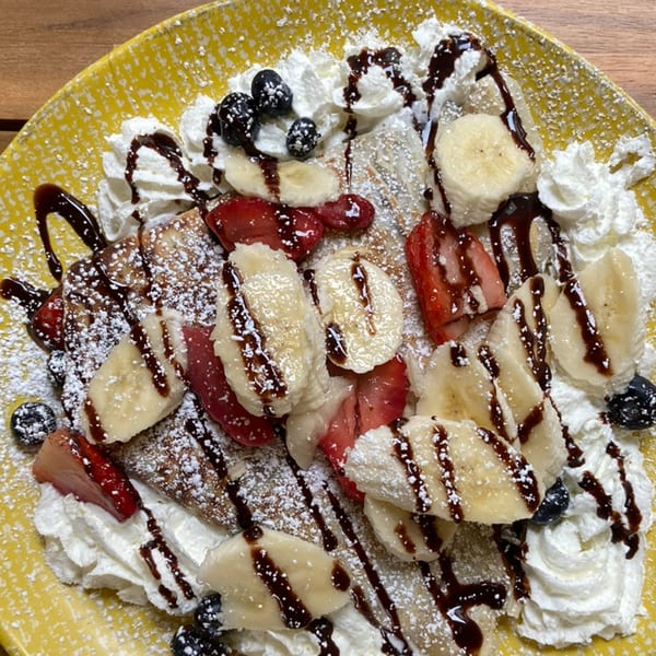 Manasiri Crepe with bananas, strawberries, blueberries, whipped cream, chocolate drizzle, and powdered sugar.